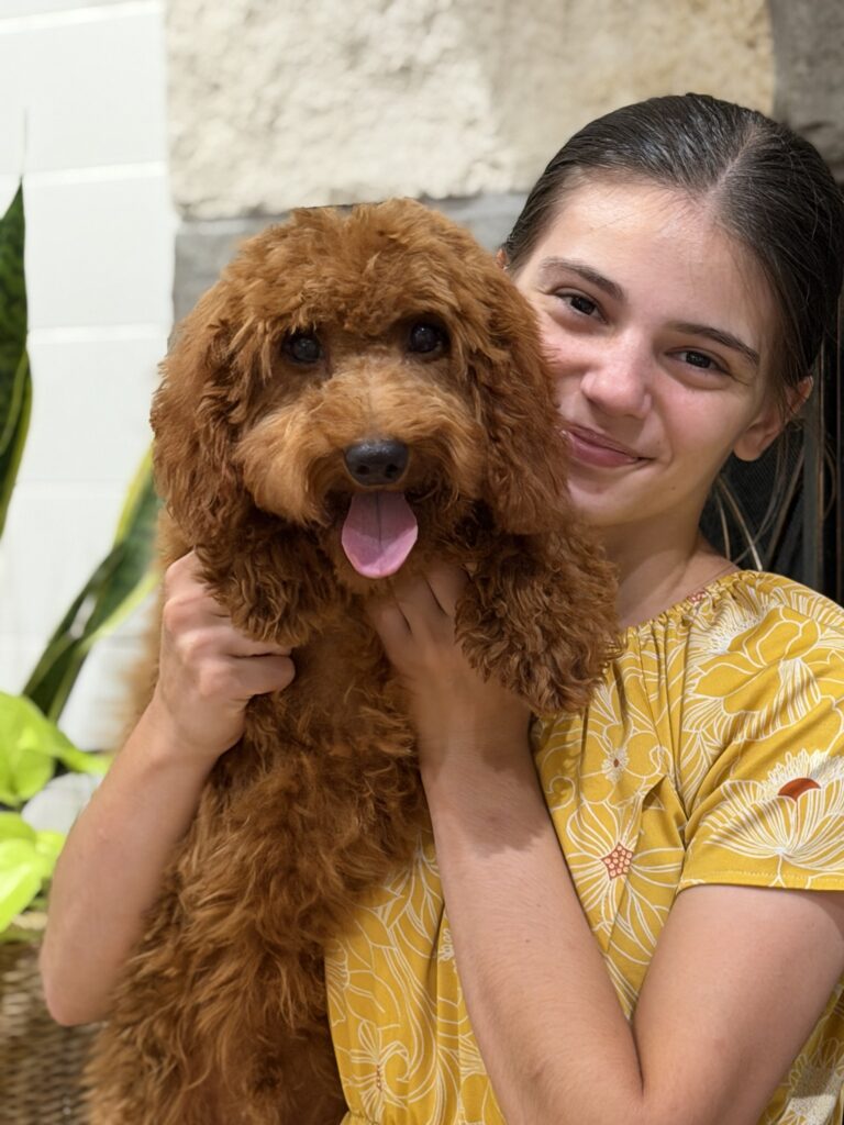 Two members of the Hidden Ranch Doodles family holding a small puppy outdoors.